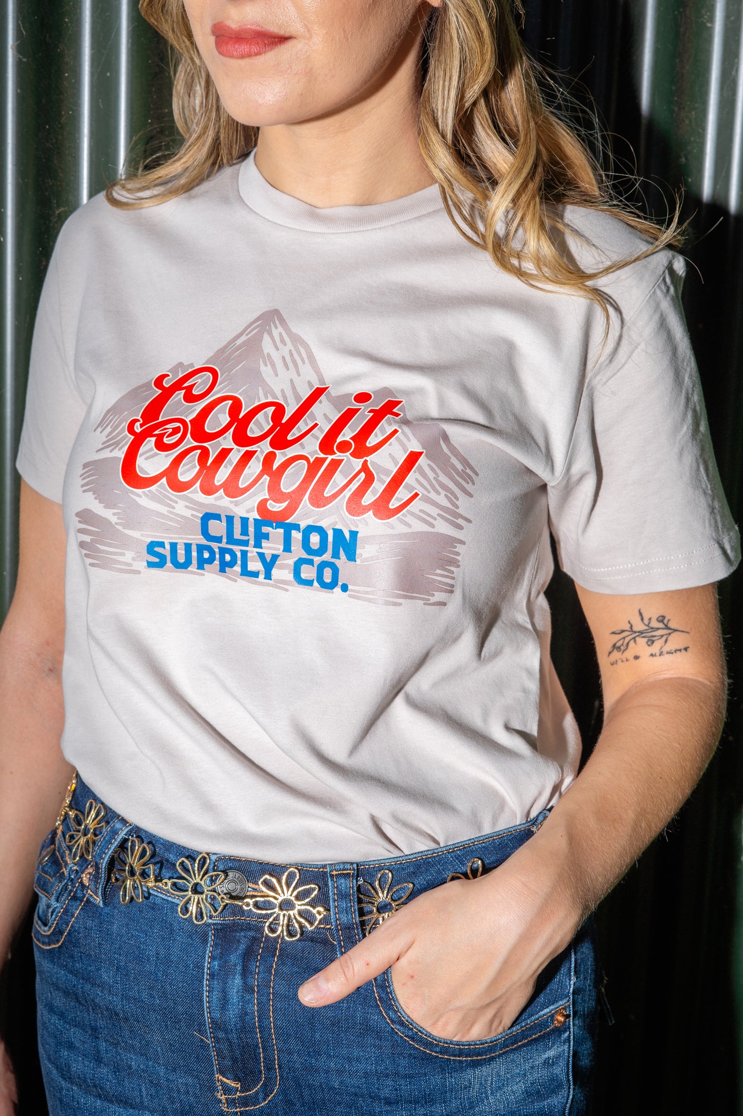 Person wearing a white t-shirt with red and blue text and graphics, standing against a dark background.